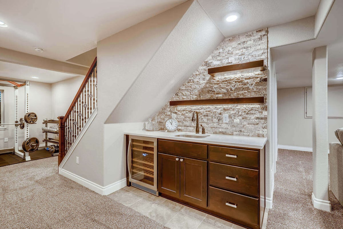 Contemporary lower-level kitchenette with dark wood cabinetry and stainless steel fridge, basement finishing project by Sheffield Homes in Arvada, CO