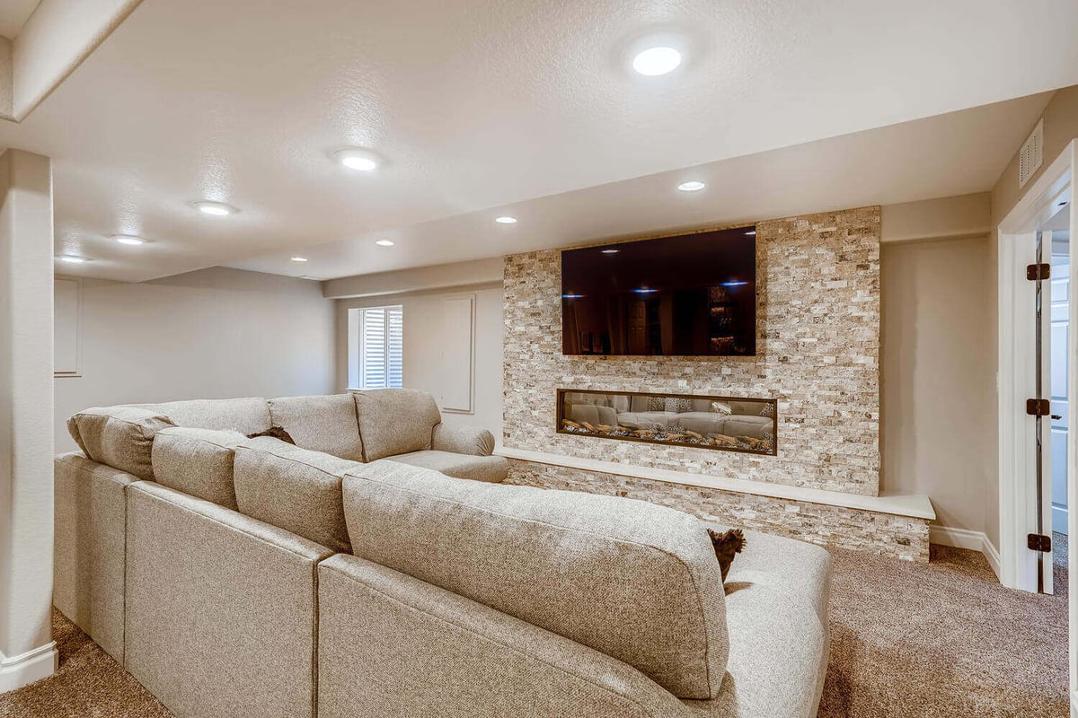 Lower-level family room with sectional sofa and fireplace, part of a basement remodel by Sheffield Homes in Arvada, CO