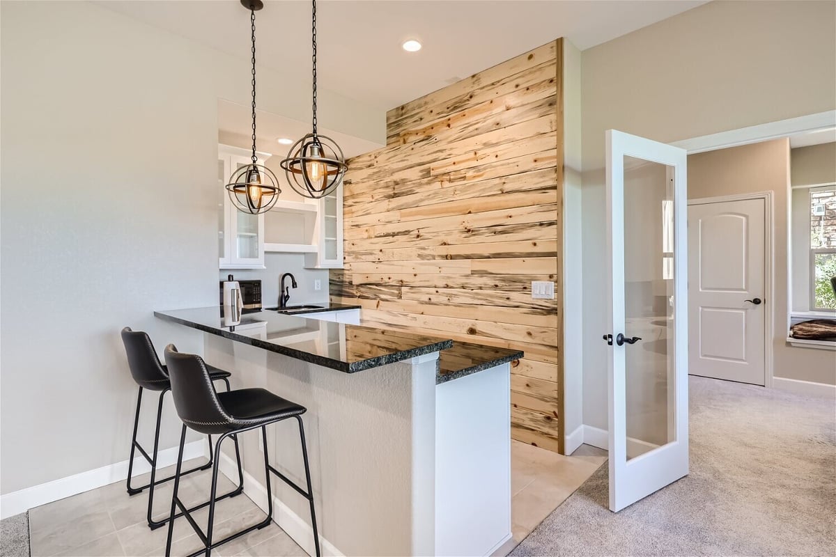 Modern kitchenette with bar seating and wood accent wall, basement renovation by Sheffield Homes in Arvada, CO