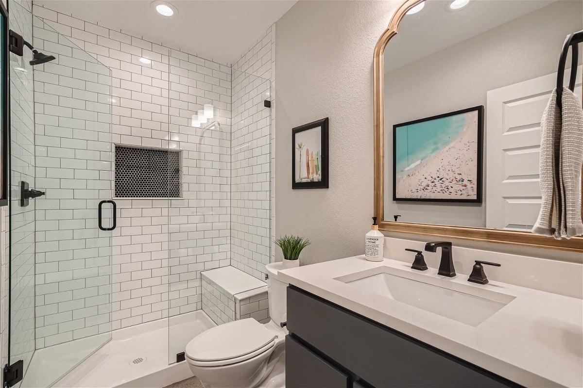 Modern lower-level bathroom with glass-enclosed shower and white subway tiles, part of a basement remodel by Sheffield Homes in Arvada, CO