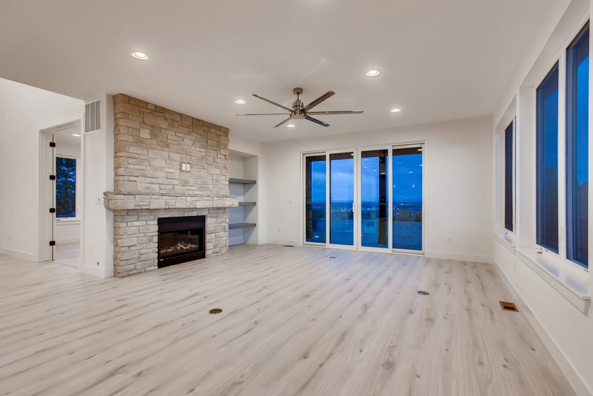 Living room with a stone fireplace and wide windows in a Sheffield Homes custom build, Arvada, CO