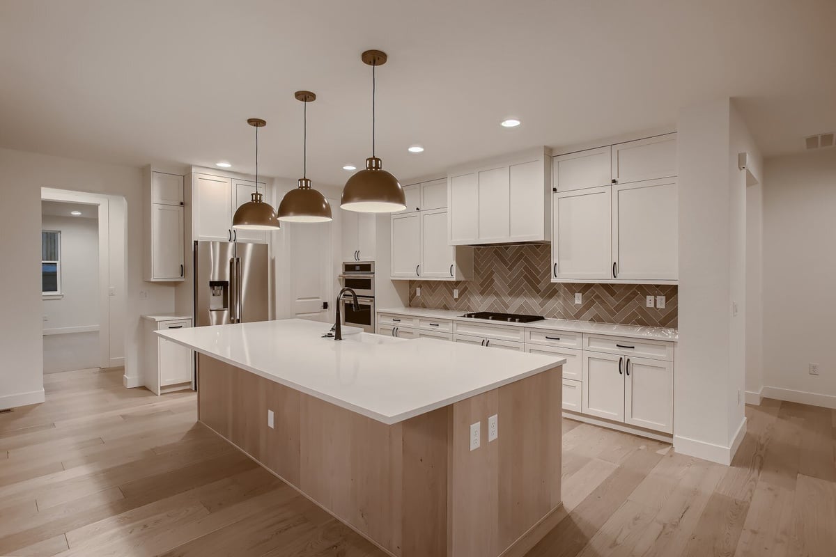 Closeup of a kitchen island with dome-shaped hanging lamps and sleek cabinetry in a custom home by Sheffield Homes, Arvada, CO