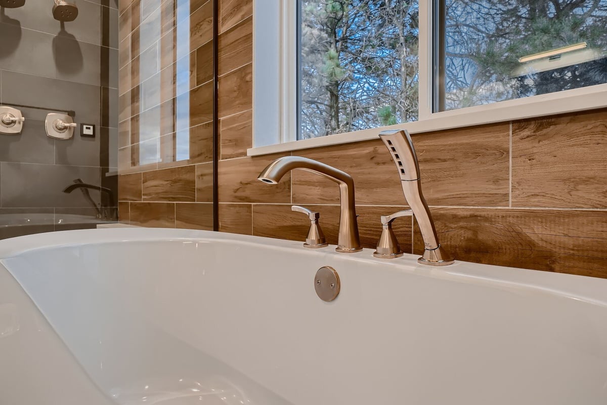 Closeup of a bathtub with a premium faucet and shower in a primary bathroom of a custom home by Sheffield Homes in Arvada, CO