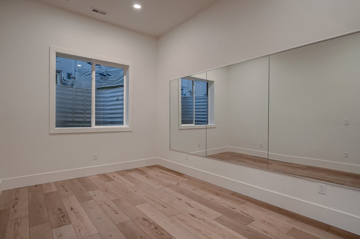 Modern and spacious lower-level exercise room with large mirrors and a window in a home by Sheffield Homes in Arvada, CO