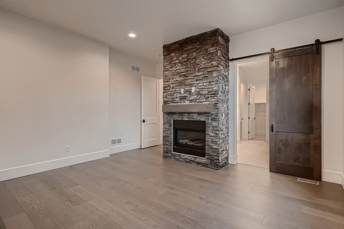 Spacious primary bedroom with a featured stone wall and fireplace in a custom home by Sheffield Homes in Arvada, CO