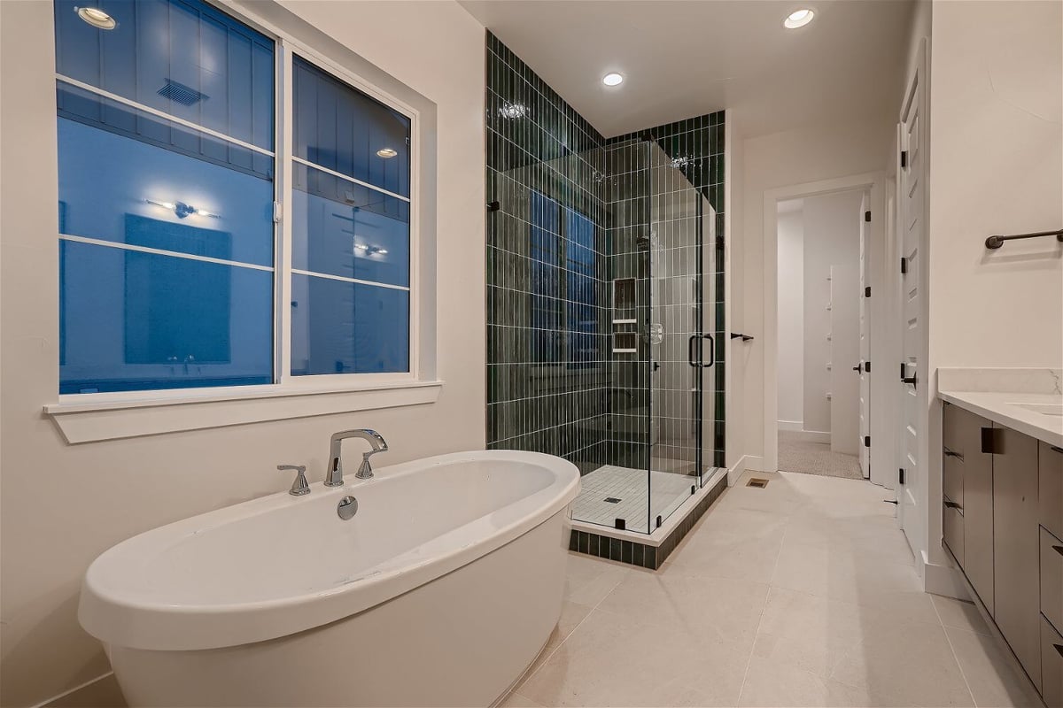 Primary bathroom with a freestanding bathtub and a shower enclosure with black tiles by Sheffield Homes in Arvada, CO