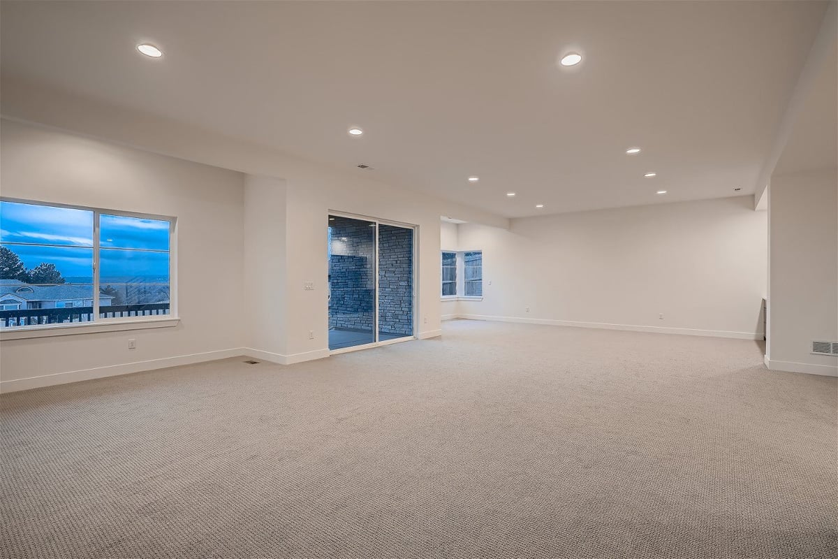 Spacious lower-level family room with carpet flooring and door for outside access by Sheffield Homes in Arvada, CO