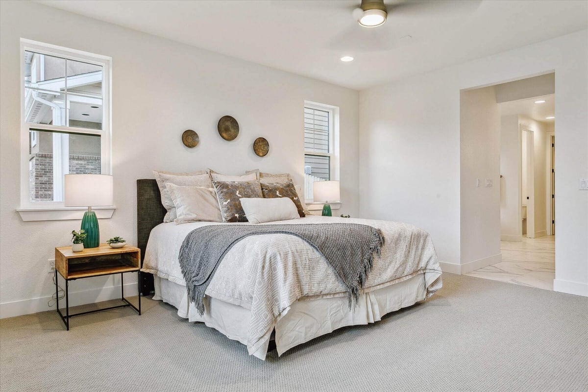 Bed and side table in a bedroom with carpet flooring and a ceiling fan in a custom home by Sheffield Homes in Arvada, CO