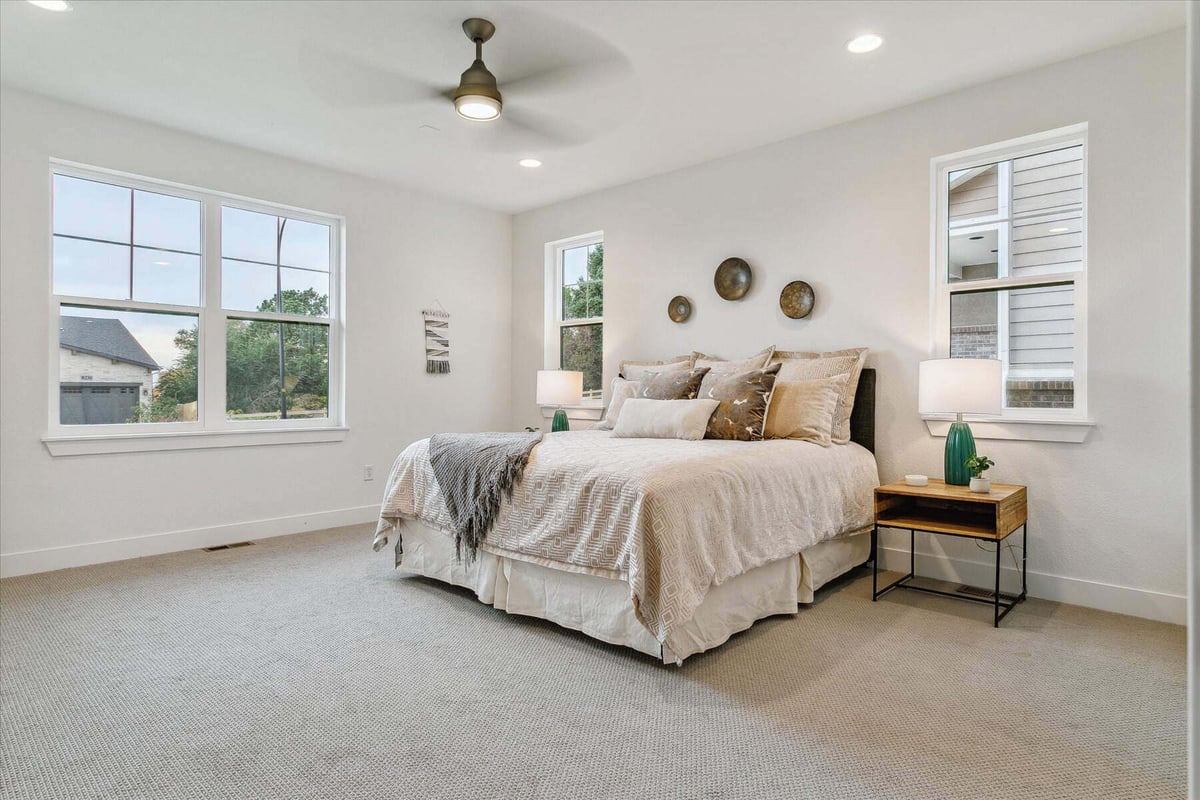 Bedroom with carpet flooring, sliding windows, a bed, and a side table in a custom home built by Sheffield Homes in Arvada, CO