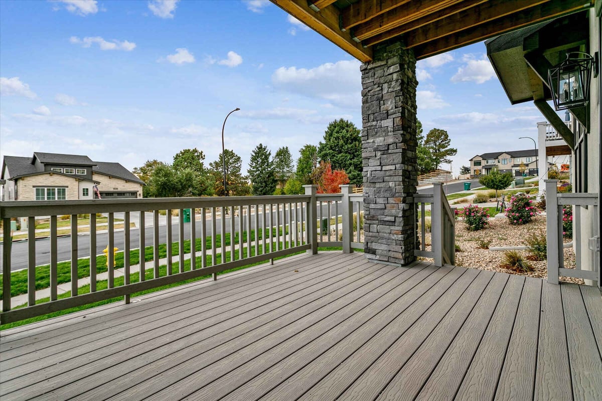 Outdoor deck off the living room with a stone accent pillar and wooden fence in a custom home by Sheffield Homes in Arvada, CO