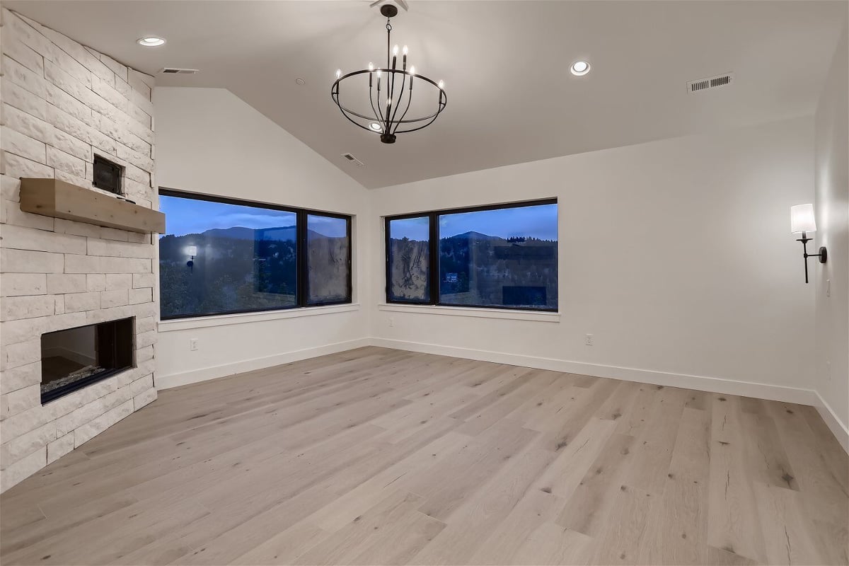 Second-floor primary bedroom with a chandelier, fireplace, and windows in a custom home by Sheffield Homes in Evergreen, CO