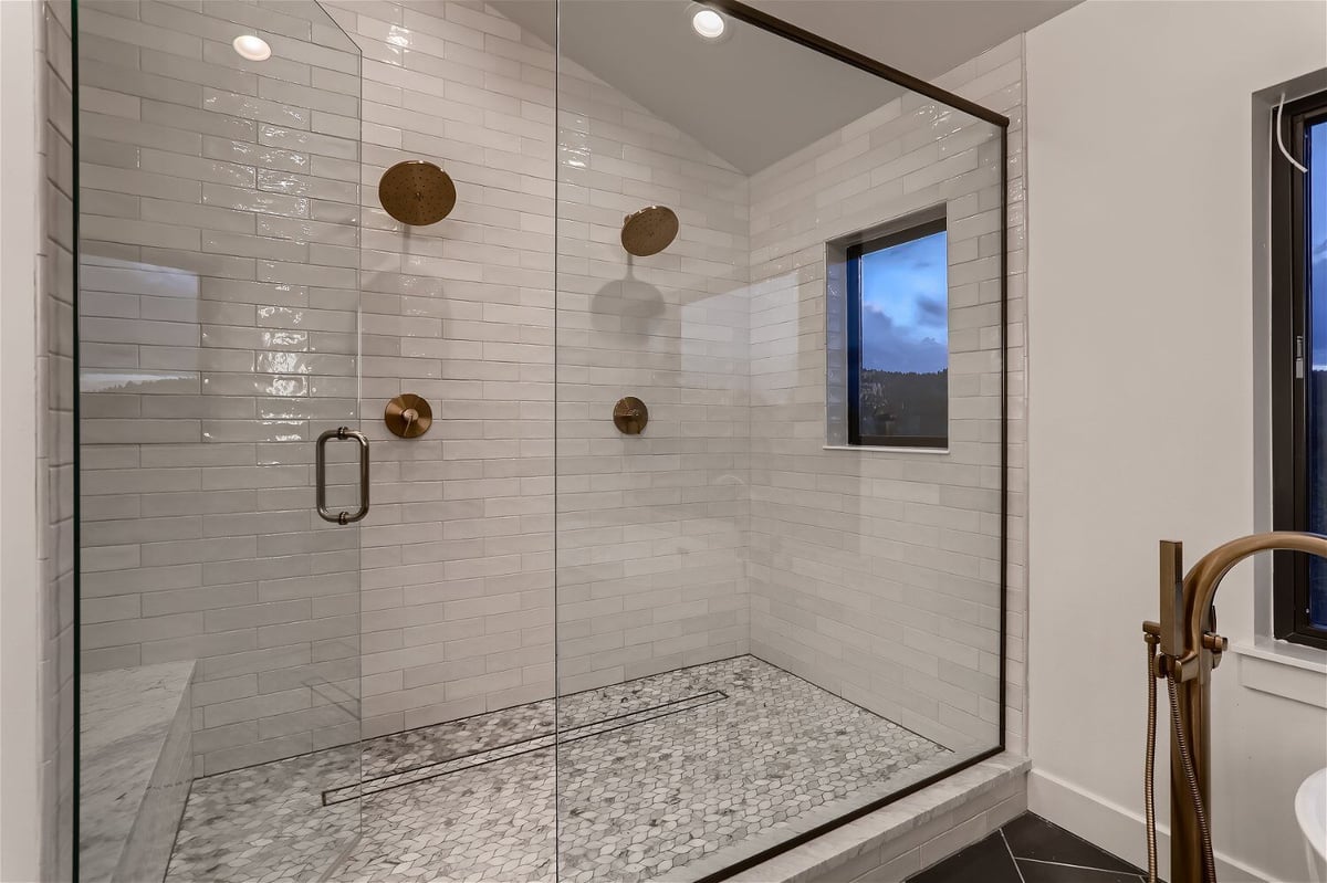 Shower enclosure with white tiling in the second-floor primary bathroom of a custom home by Sheffield Homes in Evergreen, CO