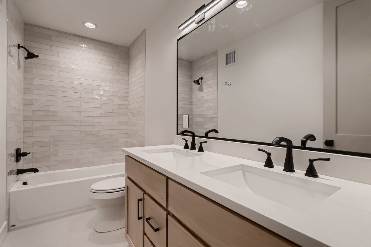 Bathroom with a bathtub, toilet, and wash basins with a large mirror in a Sheffield Homes custom home in Franktown, CO
