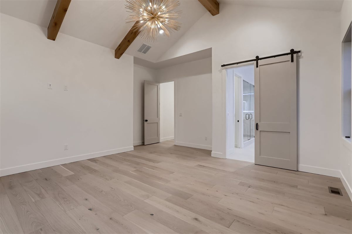 Bedroom with two doors, wooden ceiling details, and a chandelier in a custom home by Sheffield Homes in Franktown, CO