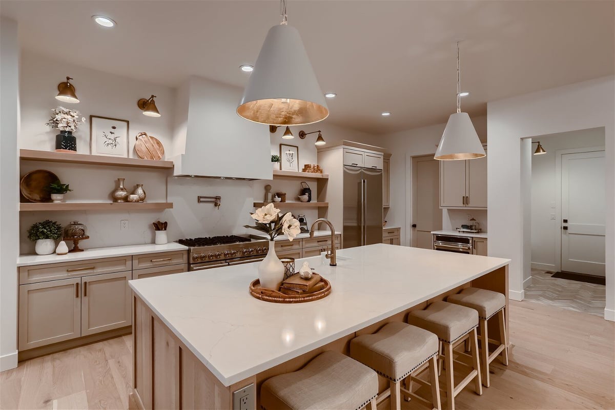 Kitchen island with dining seats and elegant lighting in an open kitchen of a custom home by Sheffield Homes in Franktown, CO
