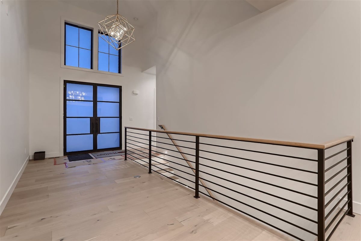 Upper-level foyer with a custom chandelier, windows, and glass doors in a custom home by Sheffield Homes in Franktown, CO