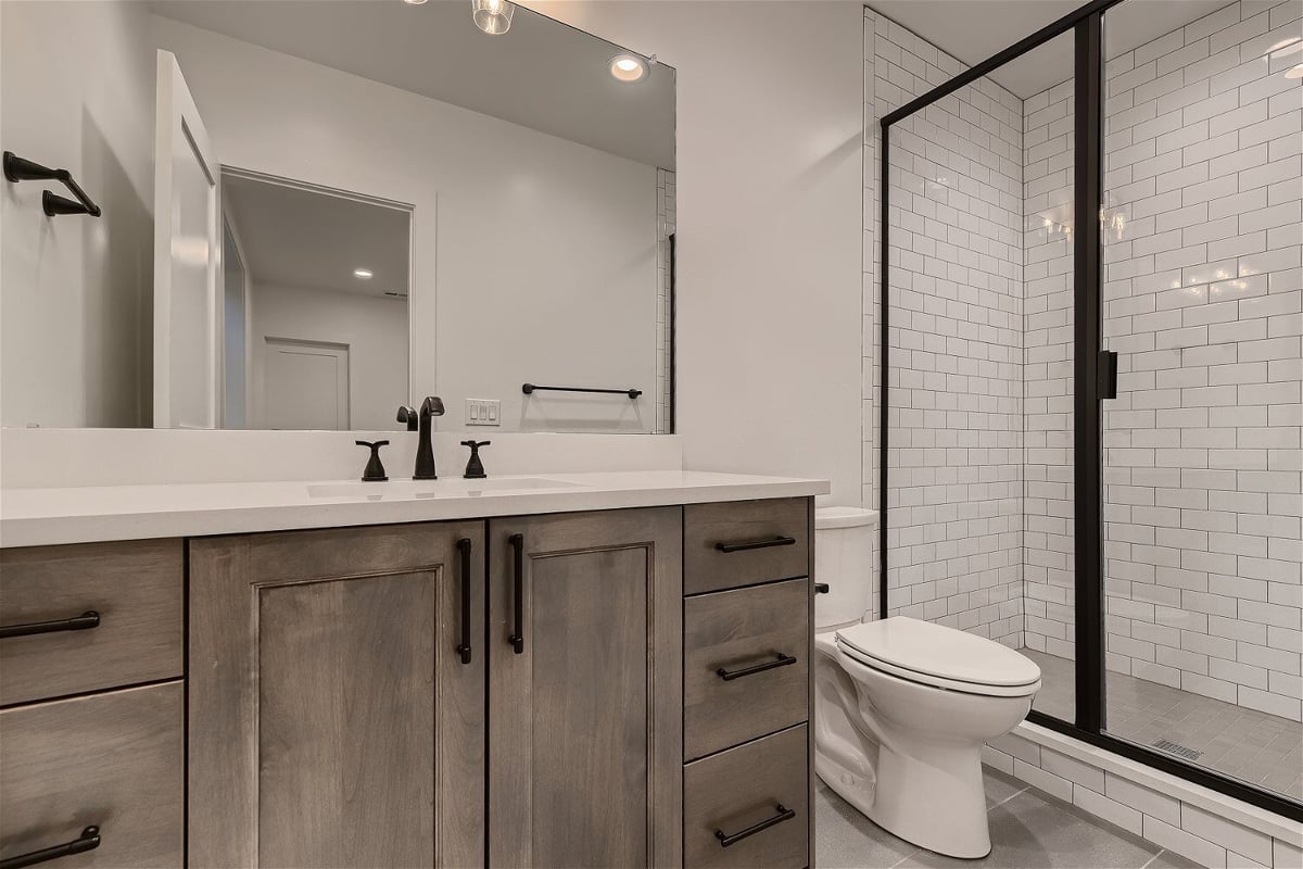 Bathroom sink with wooden cabinets next to a toilet and a shower room in a custom home by Sheffield Homes in Franktown, CO