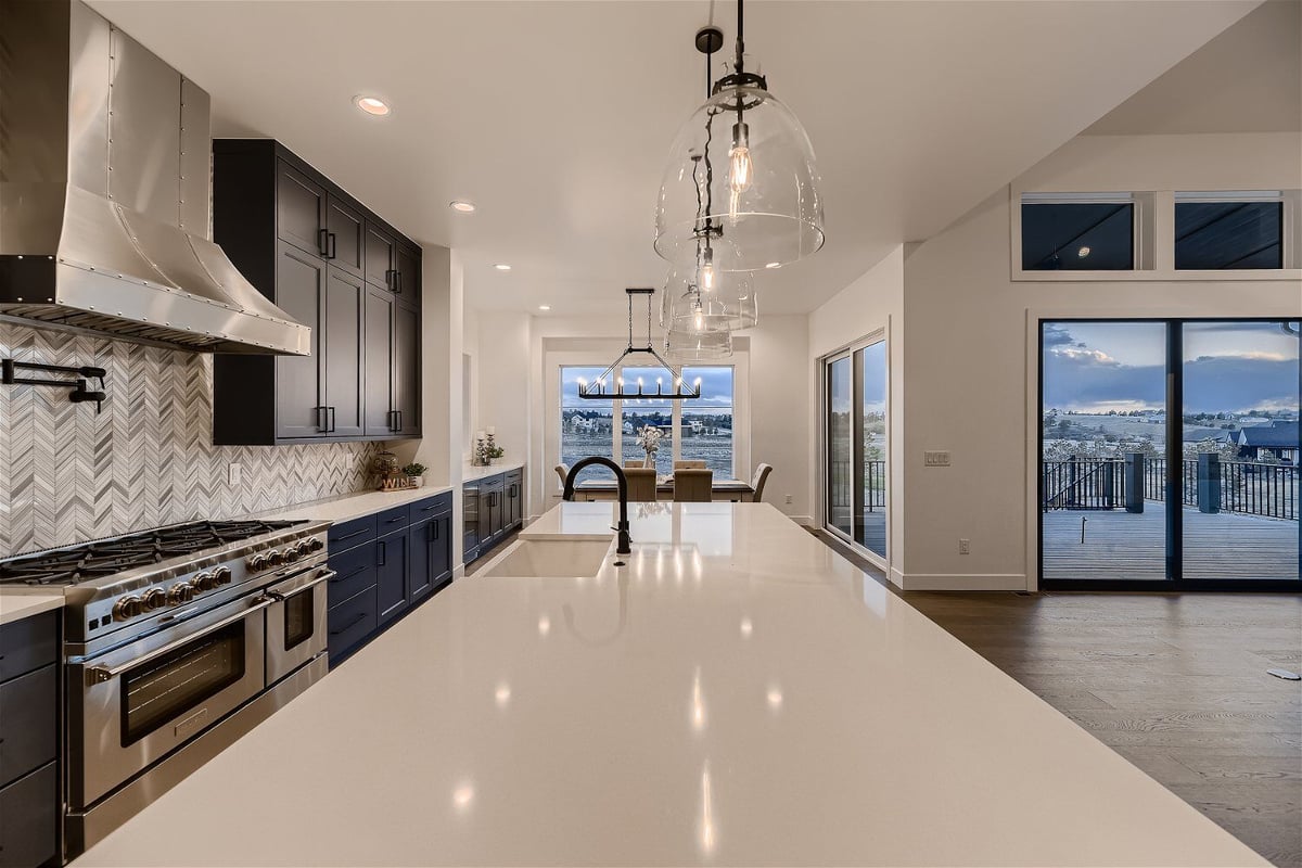 Close-up of a sleek, white-top island with elegant lighting in an open kitchen in a home by Sheffield Homes in Franktown, CO
