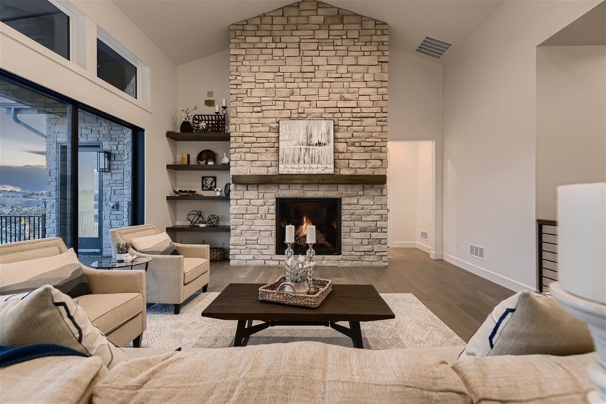 Living room with sofa sets and floor rug in front of a stone accent wall with fireplace - by Sheffield Homes in Franktown, CO