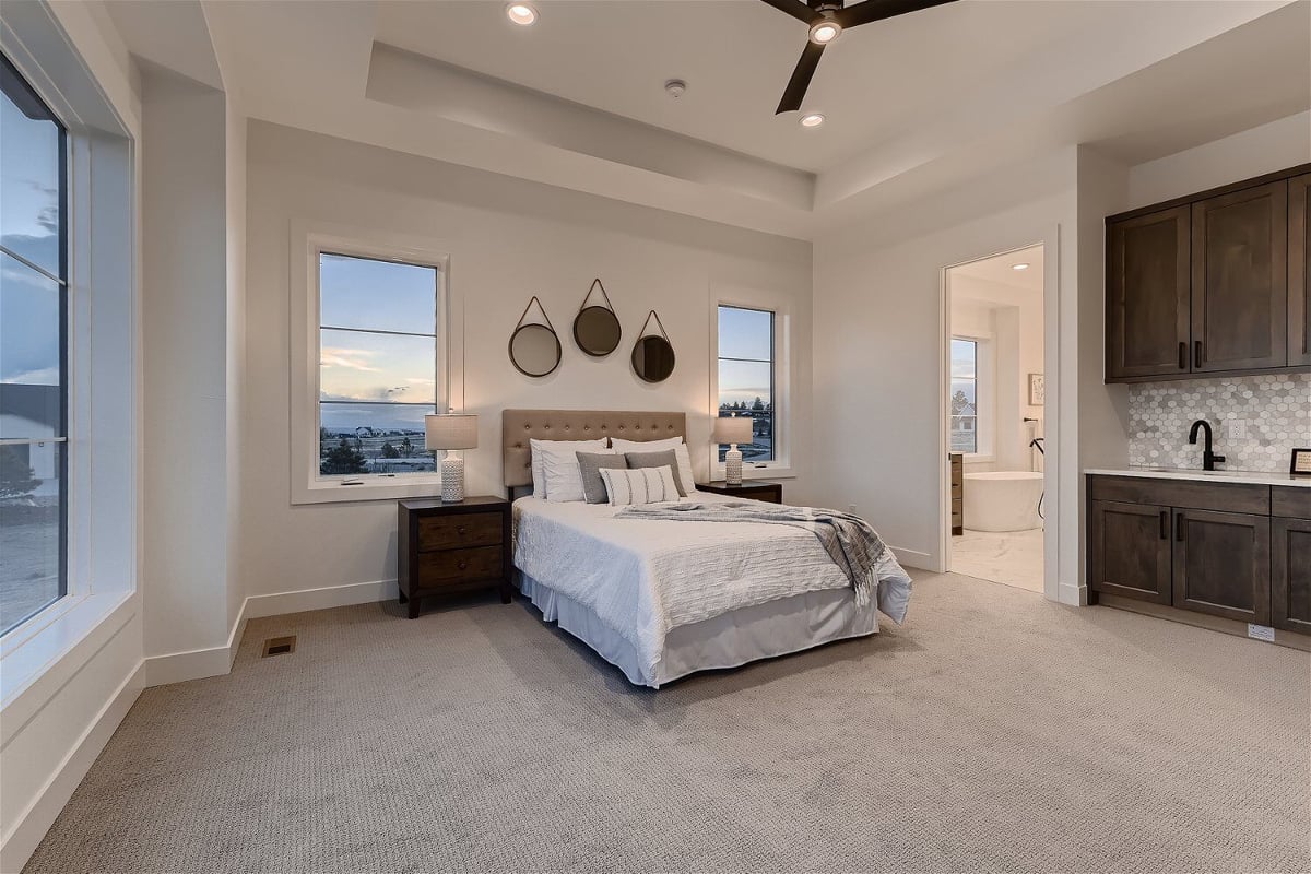 Modern primary bedroom with carpet flooring, a bar area, and an attached bath in a home by Sheffield Homes in Franktown, CO