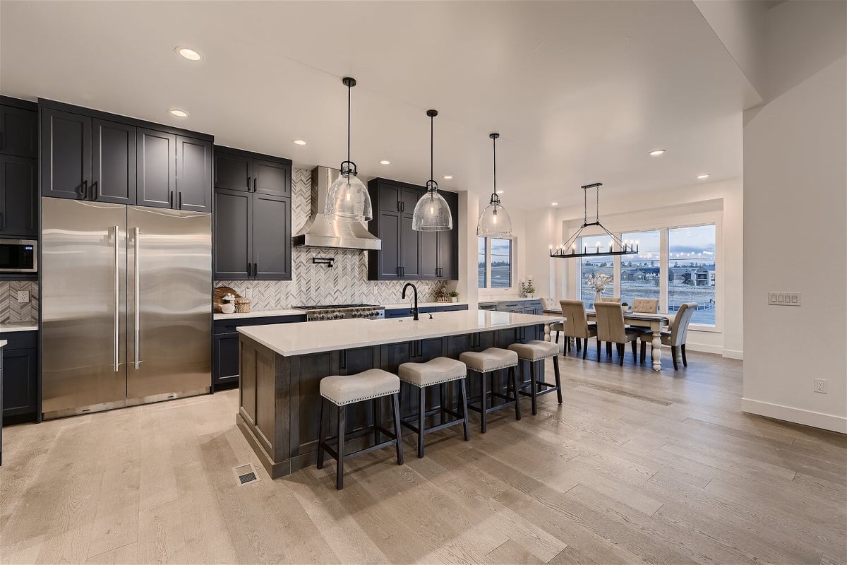 Open kitchen with an island, dining table, and sleek black cabinetry in a custom home by Sheffield Homes in Franktown, CO