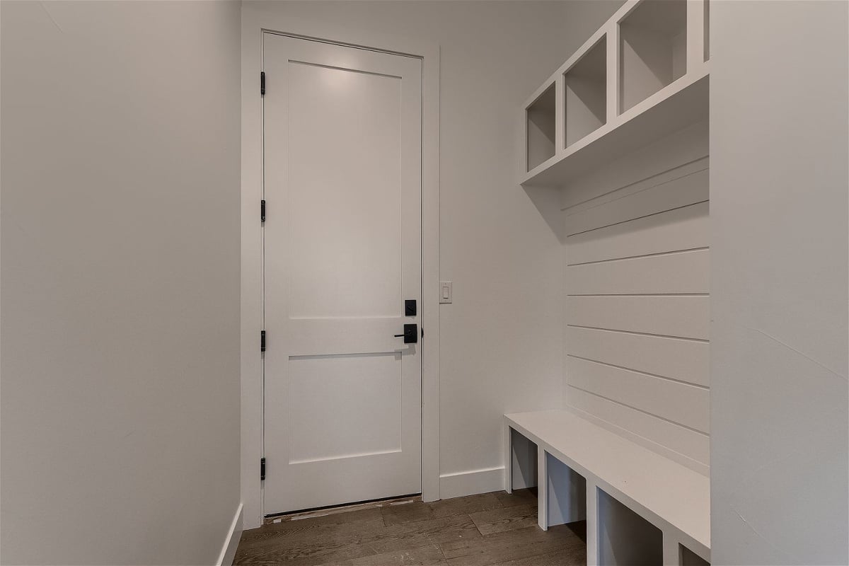 White-themed mudroom with a wooden door, a bench, and storage slots in a custom home by Sheffield Homes in Franktown, CO