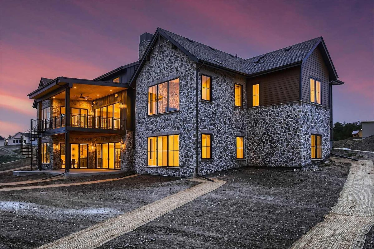 Exterior rear view of a custom home with a stone wall design and a backyard in Franktown, CO, built by Sheffield Homes