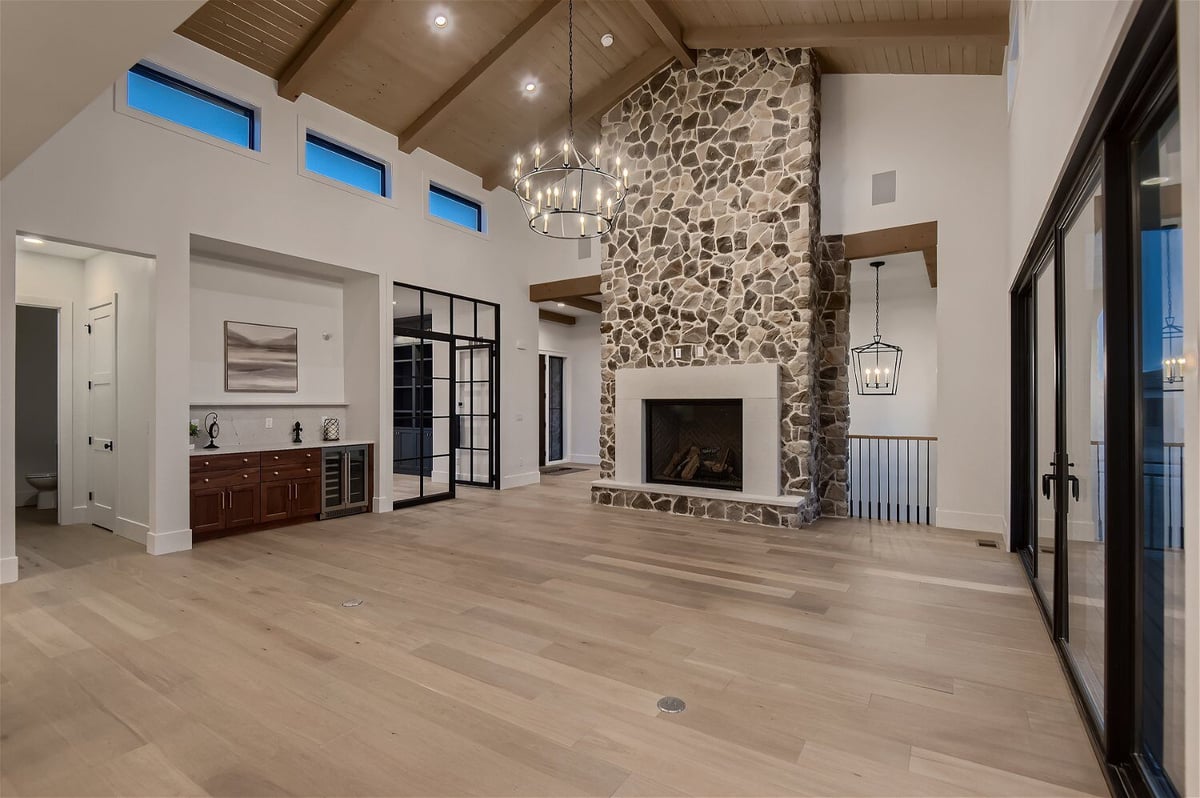 Living room with wooden ceiling craft, stone accent wall design, and a mounted fireplace by Sheffield Homes in Franktown, CO