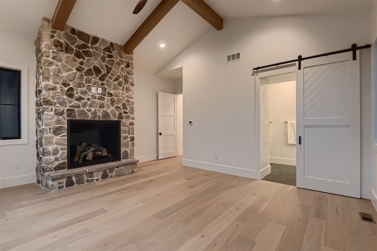 Stone accent wall with a mounted fireplace and white doors in a bedroom of a custom home by Sheffield Homes in Franktown, CO