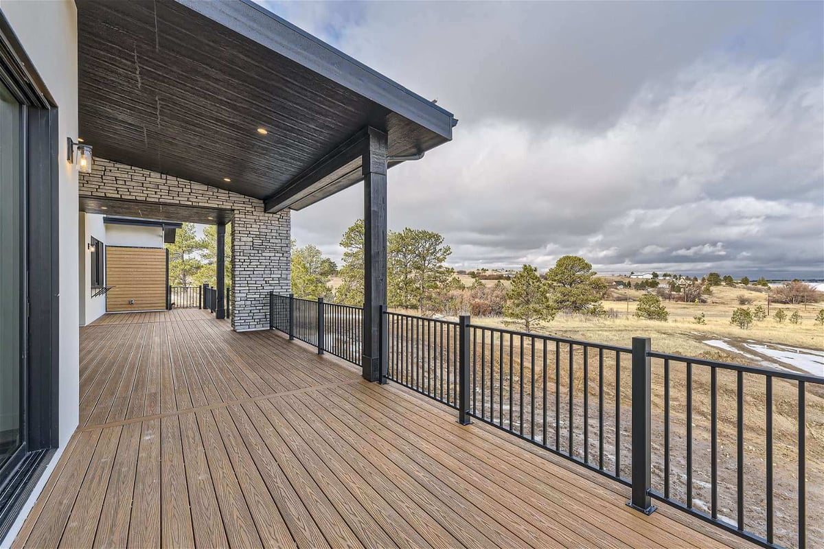 Balcony with a black metal fence, wooden top deck, and stone accent pillar beam in a home by Sheffield Homes in Franktown, CO