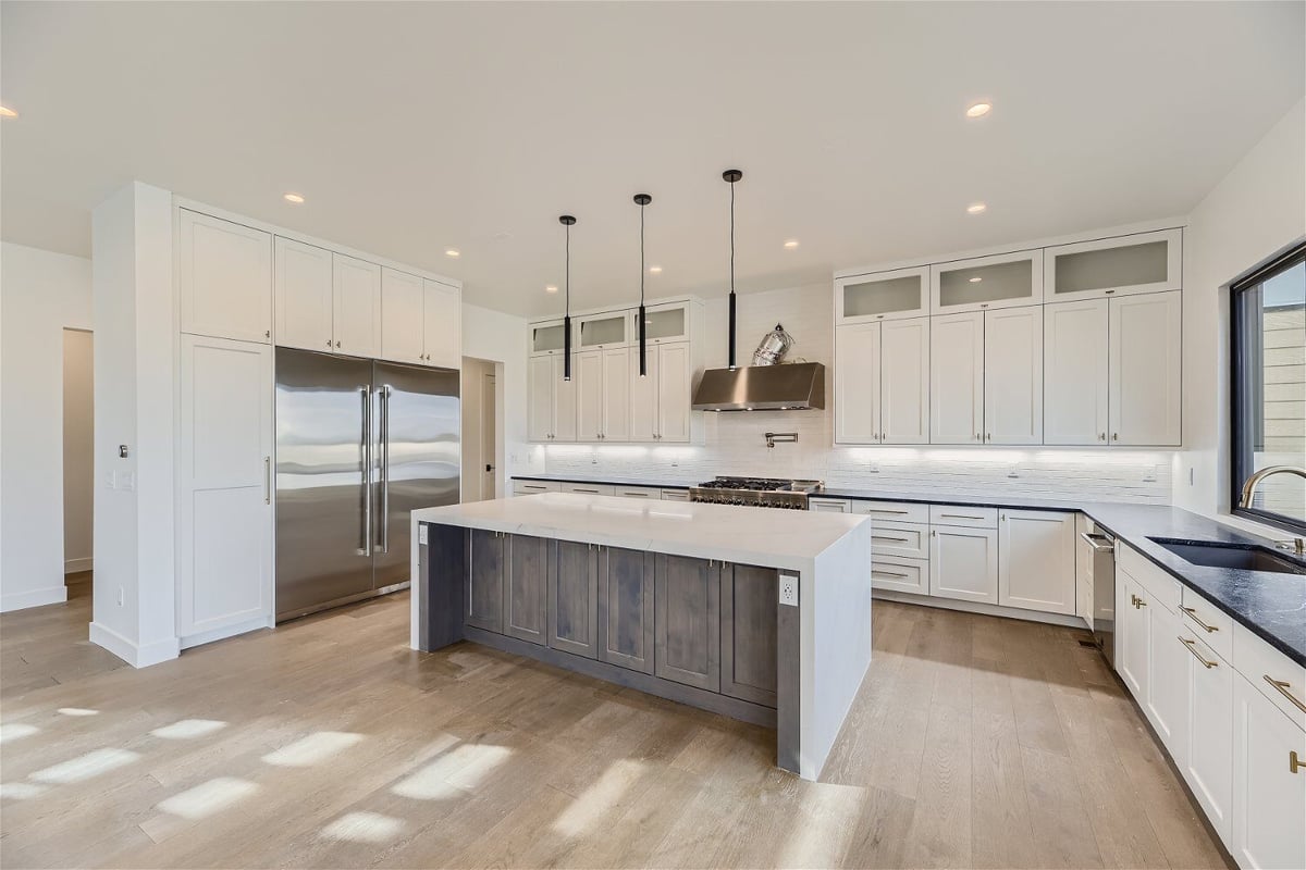 Kitchen with an island, kitchen appliances, and white cabinetry in a custom home by Sheffield Homes in Franktown, CO