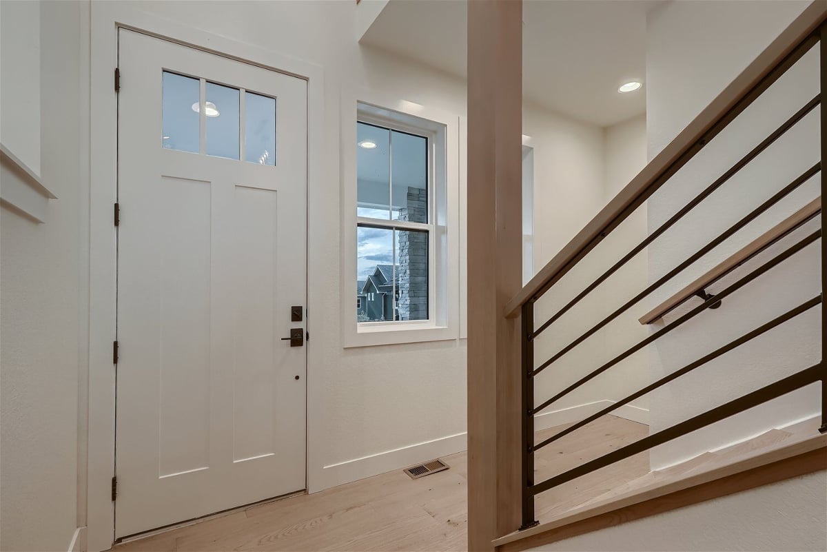 Foyer with metal railings and a wooden beam in front of a white door in a custom home by Sheffield Homes in Louisville, CO