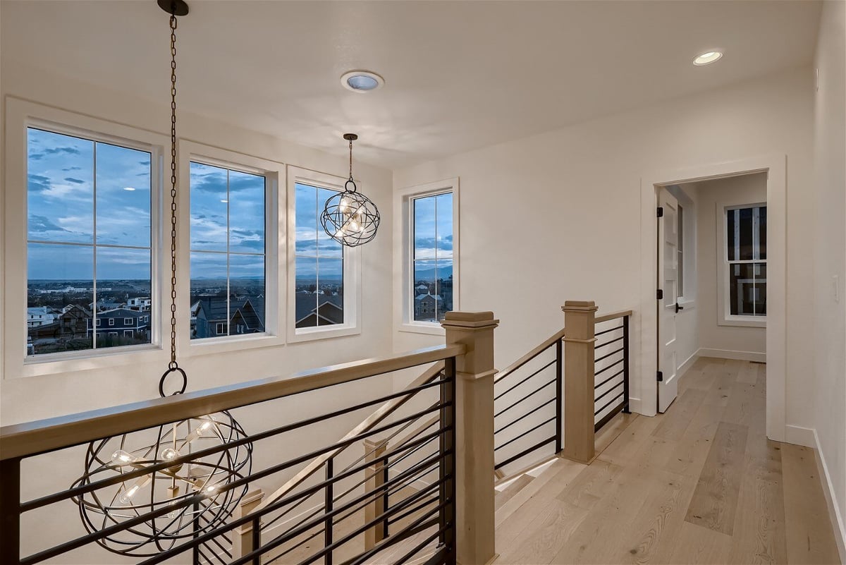 Hallway featuring a staircase with railings and two elegant chandeliers in a custom home by Sheffield Homes in Louisville, CO