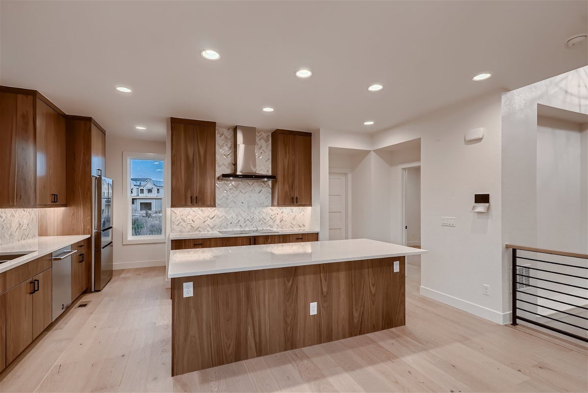 Open kitchen with sleek countertop island and natural wood cabinetry in a custom home by Sheffield Homes in Louisville, CO