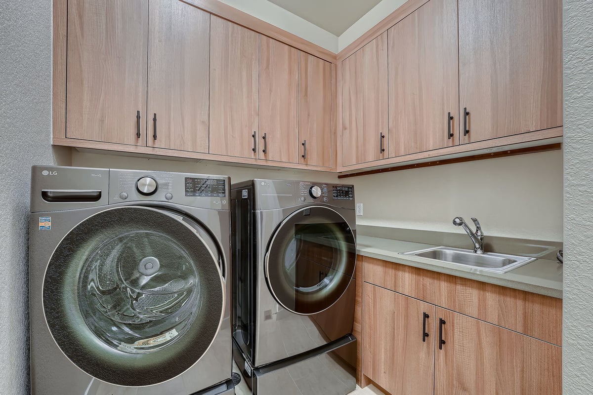 Laundry room with modern washer and dryer and wood cabinets in a Sheffield Homes Denver custom home