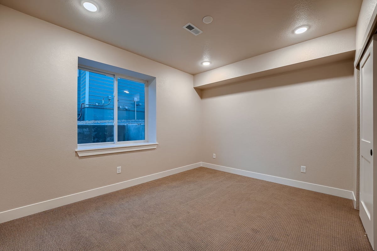 Lower level bedroom with carpeted flooring and large window in a Denver custom home by Sheffield Homes