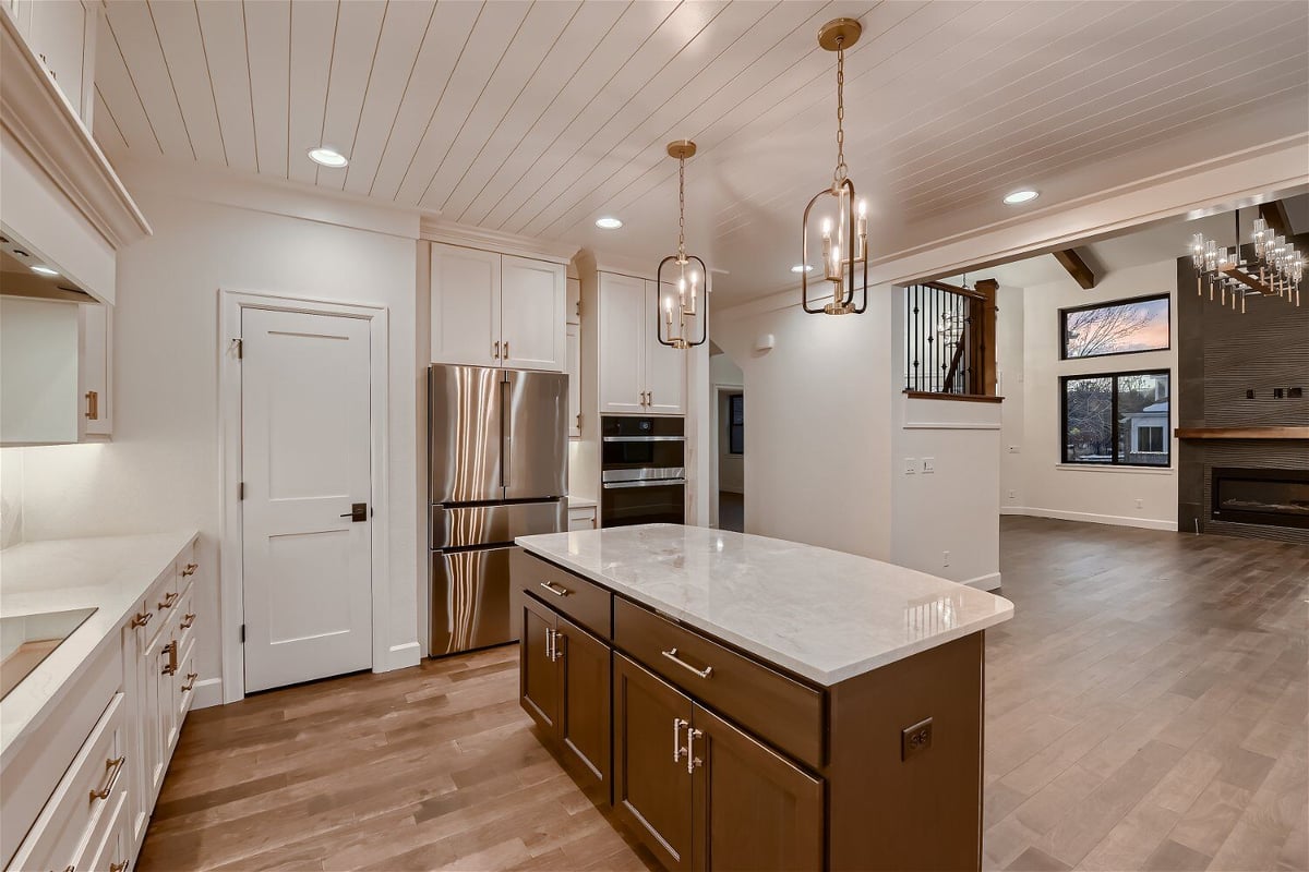 Island with a marble countertop, wooden base, and cabinetry in a custom home kitchen by Sheffield Homes in Louisville, CO