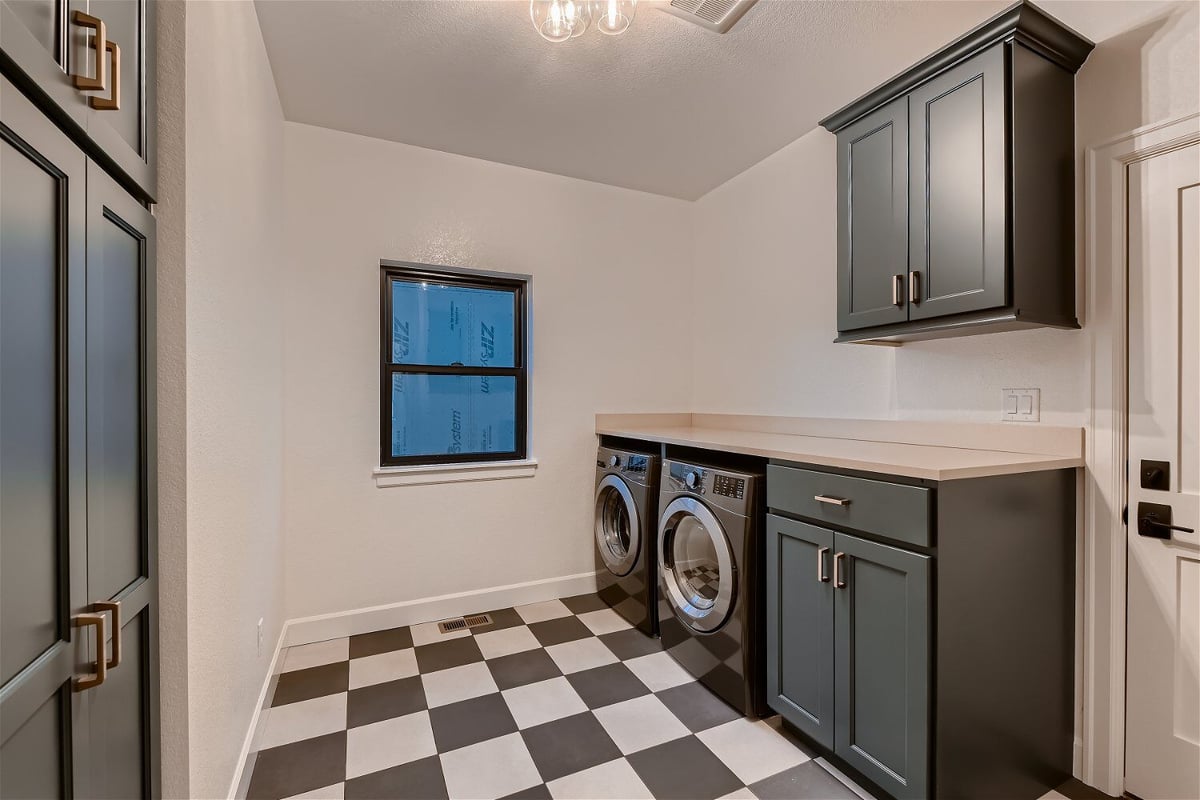 Laundry room with checked floor design, forest green cabinets, and washing machines in a Sheffield Homes home, Louisville, CO