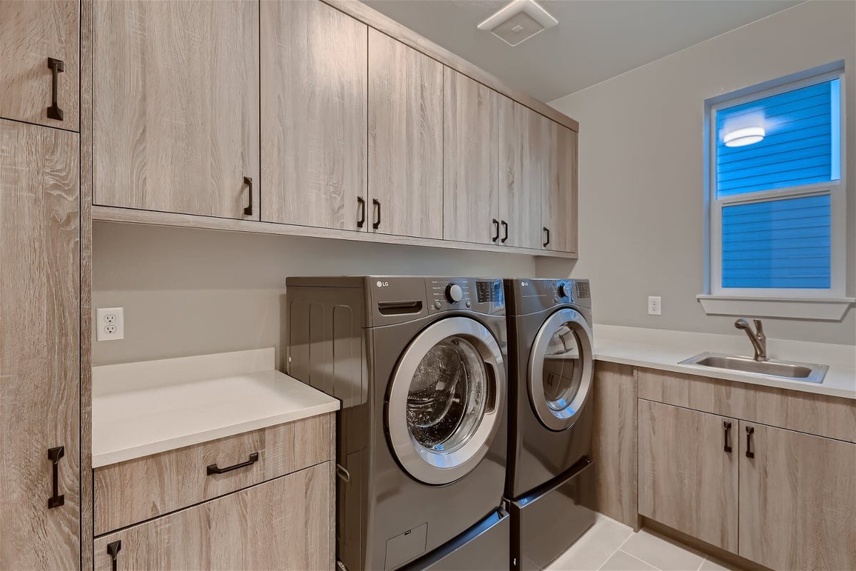 Laundry room with washing machines and wooden cabinets for storage in a custom home by Sheffield Homes in Louisville, CO