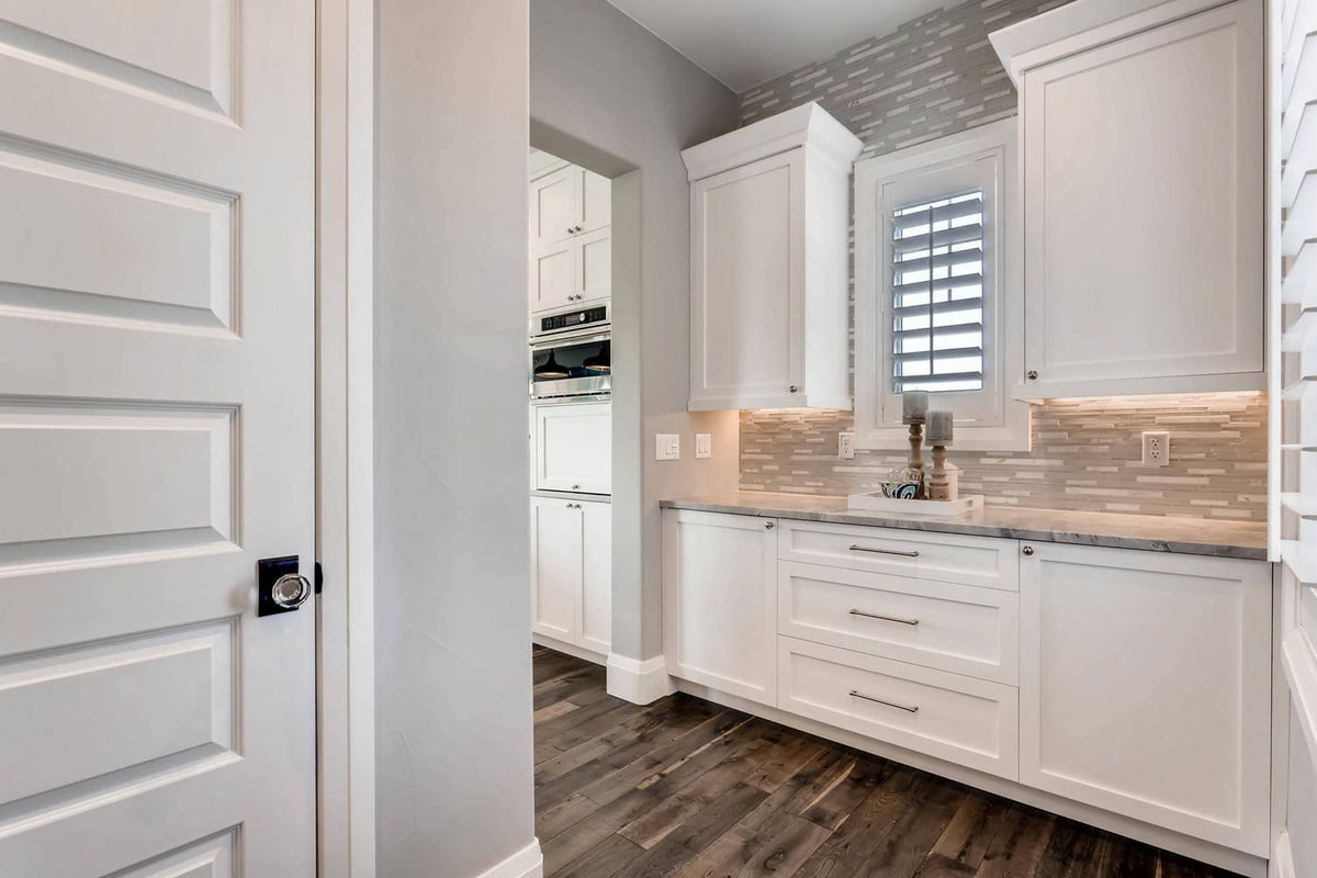 Butler_s pantry with wooden texture flooring and white cabinetry for storage in a custom home by Sheffield Homes, Parker, CO