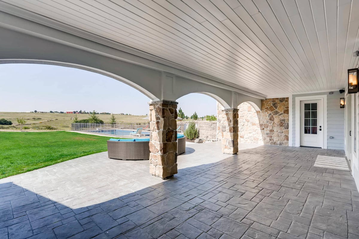 Custom patio with stone accent pillars adjacent to a beautiful outdoor lawn of a custom home by Sheffield Homes in Parker, CO