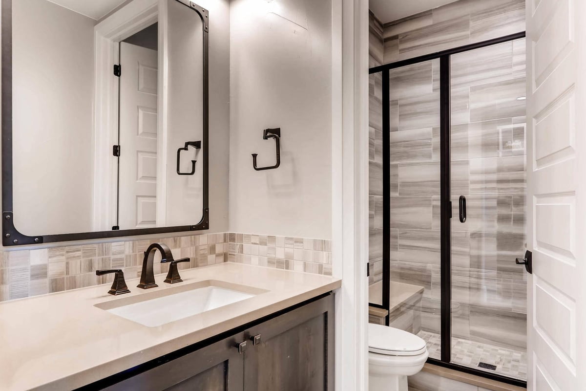 Lower-level bathroom with a vanity, toilet, and a premium glass-enclosed shower in a home by Sheffield Homes in Parker, CO