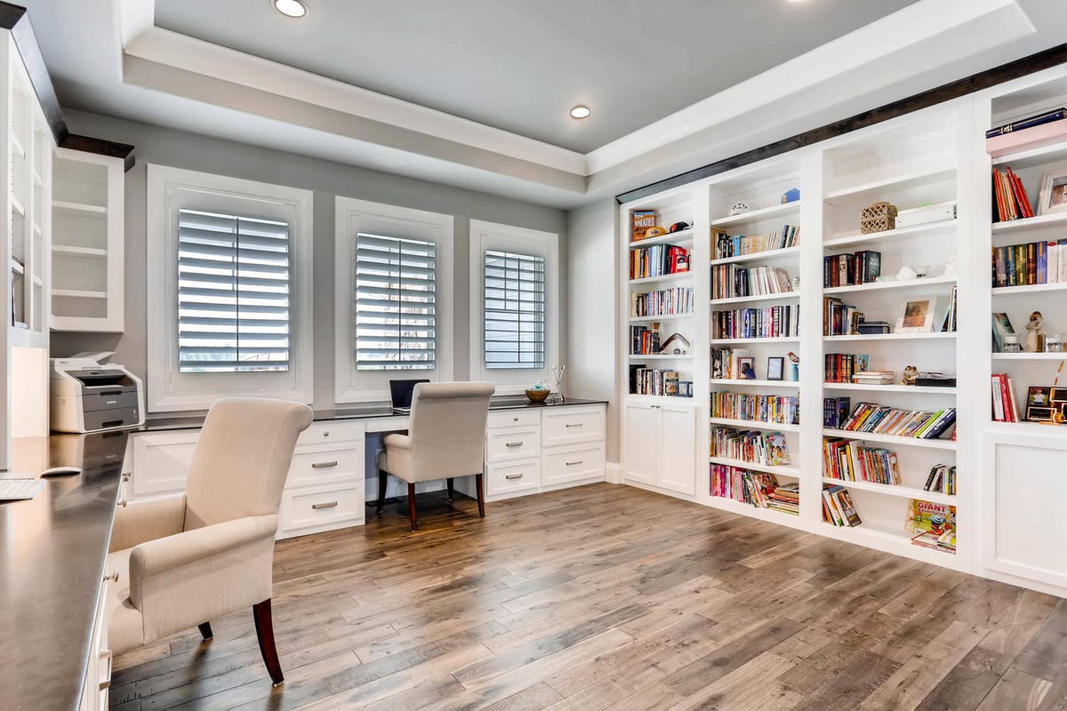 Modern office with bookshelves, multiple workstations, and white cabinetry in a custom home by Sheffield Homes in Parker, CO