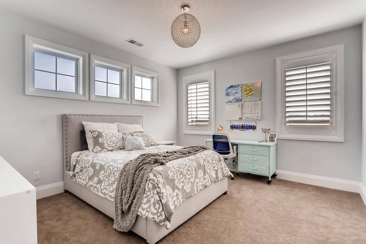 Second-floor bedroom with carpet floor, a side dresser, and windows for ventilation in a Sheffield Homes home in Parker, CO