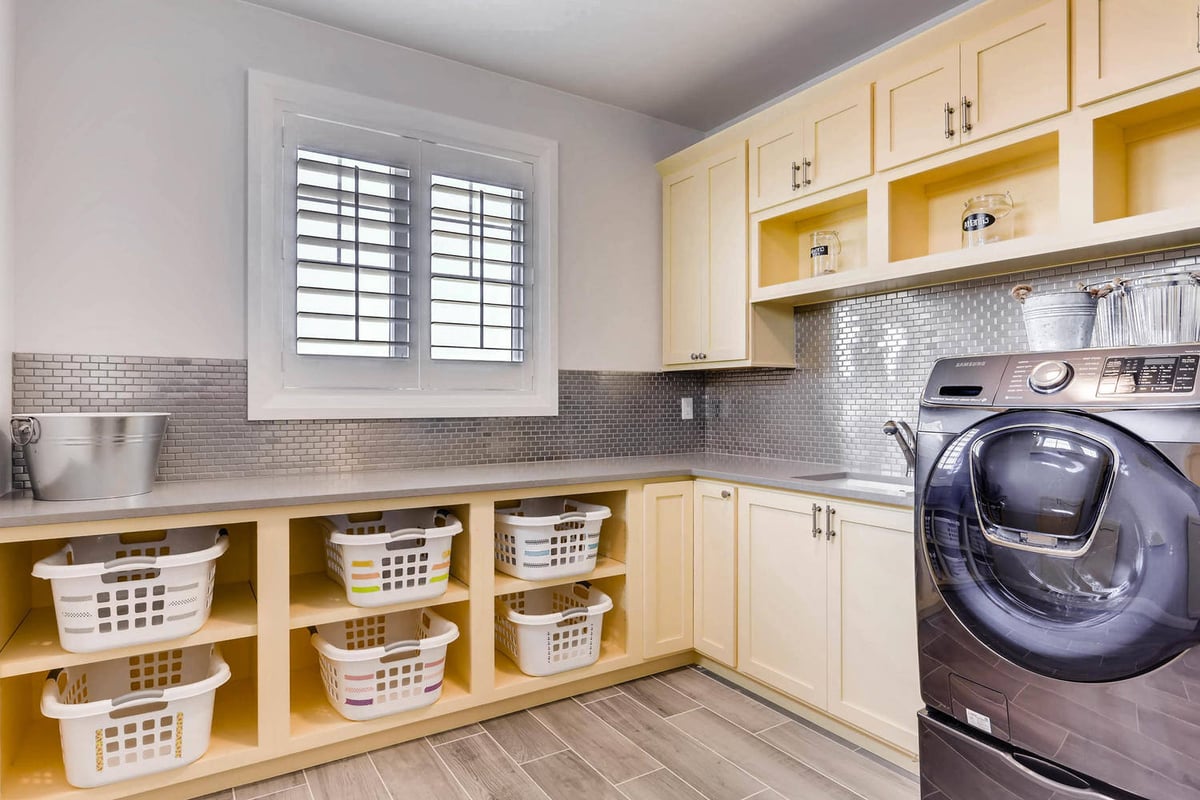 Second-floor laundry room with beige cabinetry, plastic baskets, and a washing machine in a Sheffield Homes home, Parker, CO