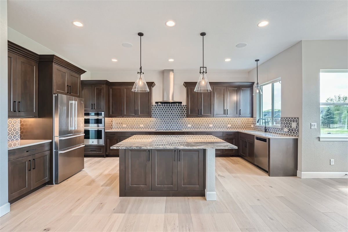 Front view of the open kitchen with light fixtures, wooden cabinetry, and modern design by Sheffield Homes in Superior, CO