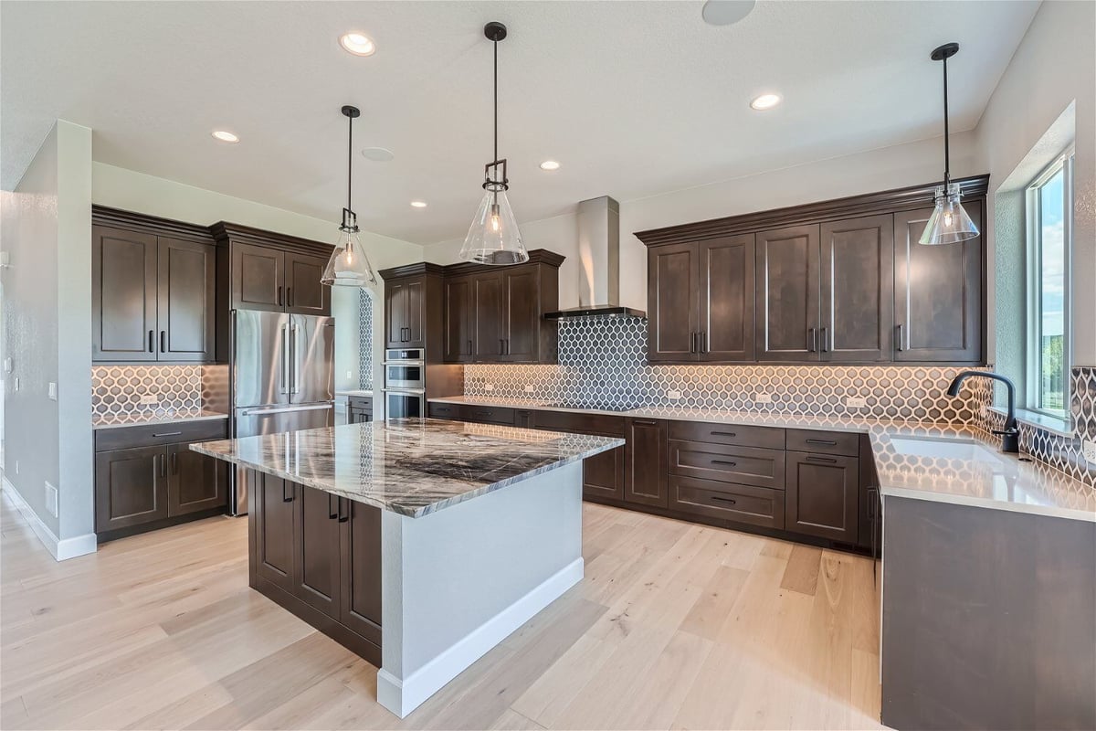 Open kitchen with elegant pendant lighting fixtures and wooden cabinetry in a custom home by Sheffield Homes in Superior, CO