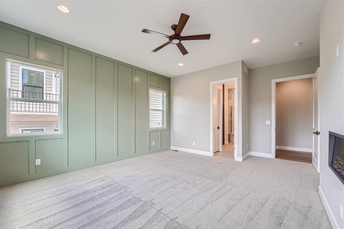 Primary bedroom with a green wall design, a ceiling fan, and a fireplace in a custom home by Sheffield Homes in Superior, CO