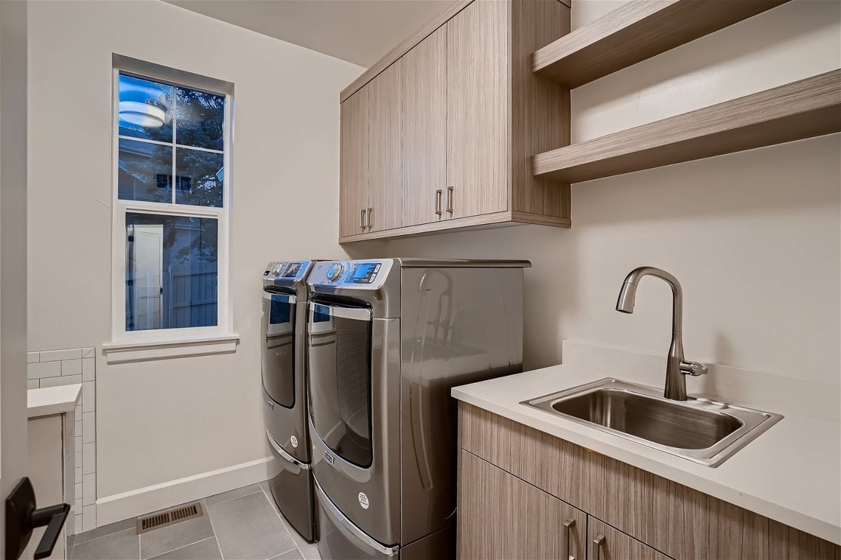 Compact laundry room with washing machines, a wash sink, and cabinetry for storage in a Sheffield Homes home in Superior, CO