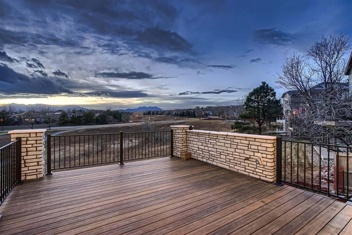 Deck with a metal fence and stone accent columns, offering expansive outdoor views from a Sheffield Homes home, Superior, CO